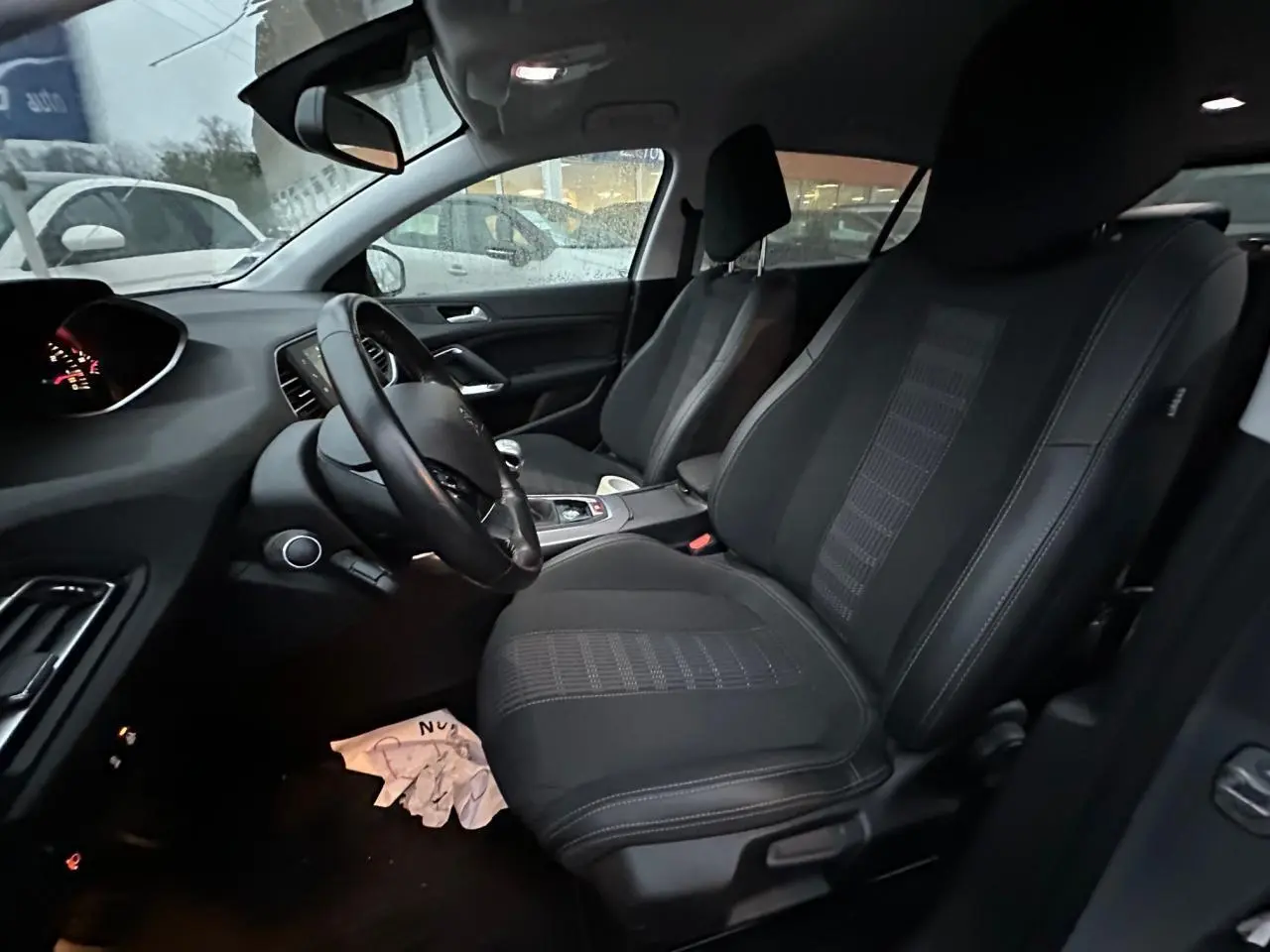 Vue intérieure côté conducteur de la Peugeot 308 gris Artense, montrant sièges avant en tissu et tableau de bord moderne.