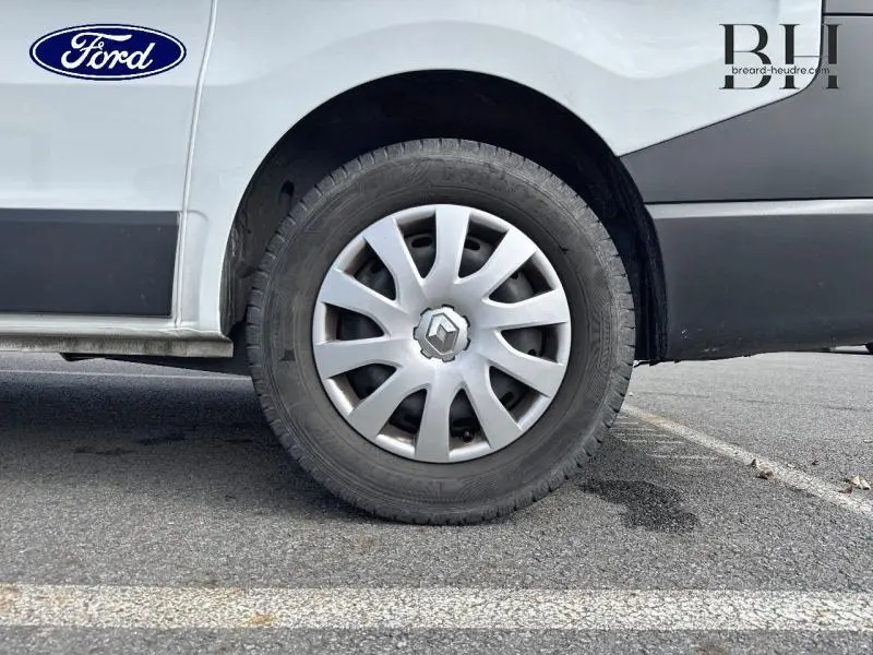 Gros plan sur la roue arrière droite d’un Renault Trafic blanc glacier avec enjoliveur et habillage latéral noir.