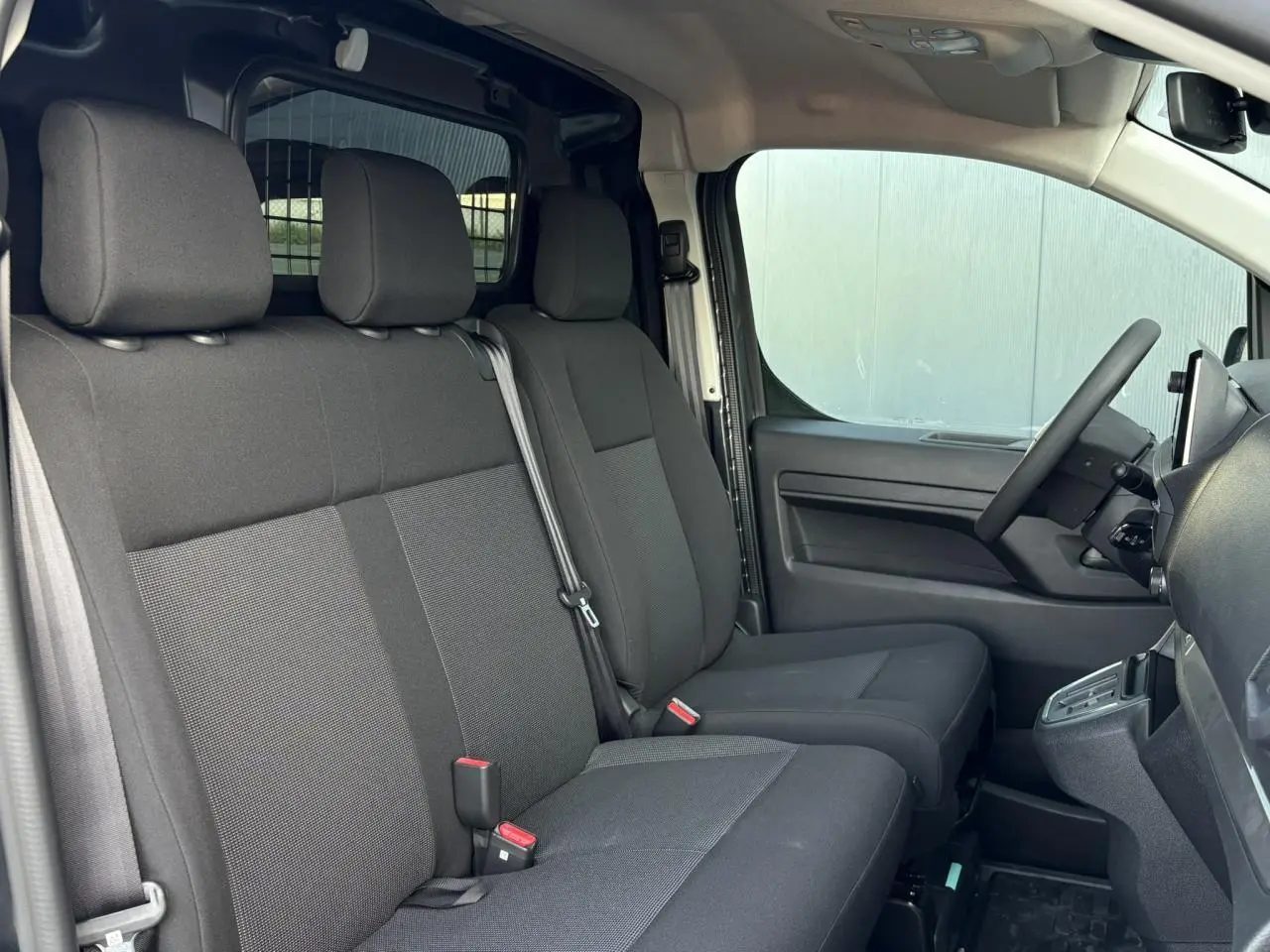 Vue intérieure côté conducteur du Citroën Jumpy gris, montrant les sièges avant et la cloison vitrée isolante derrière.