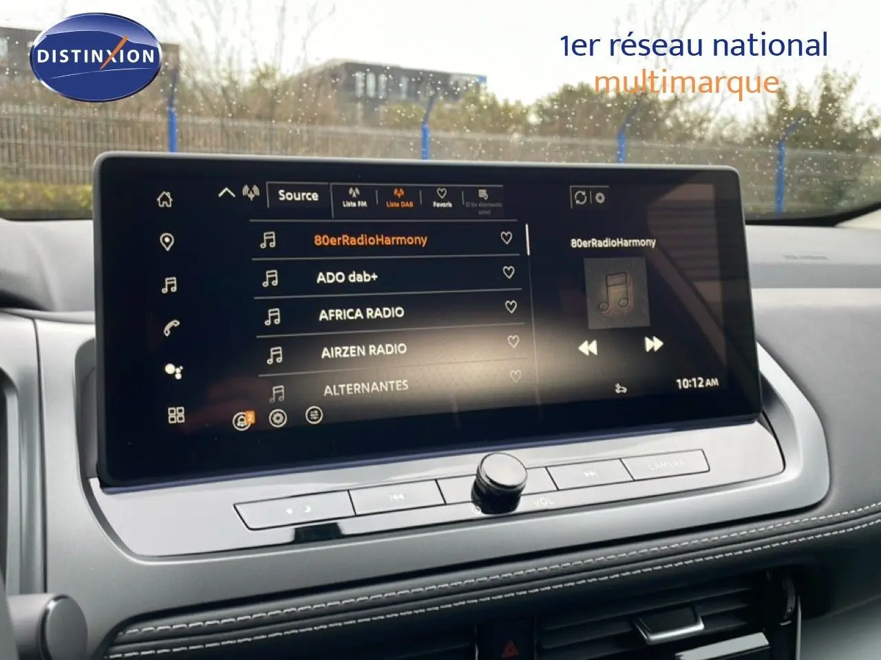 Vue intérieure centrée sur l'écran tactile multimédia du Nissan Qashqai blanc nacré 2025, affichant les stations radio.