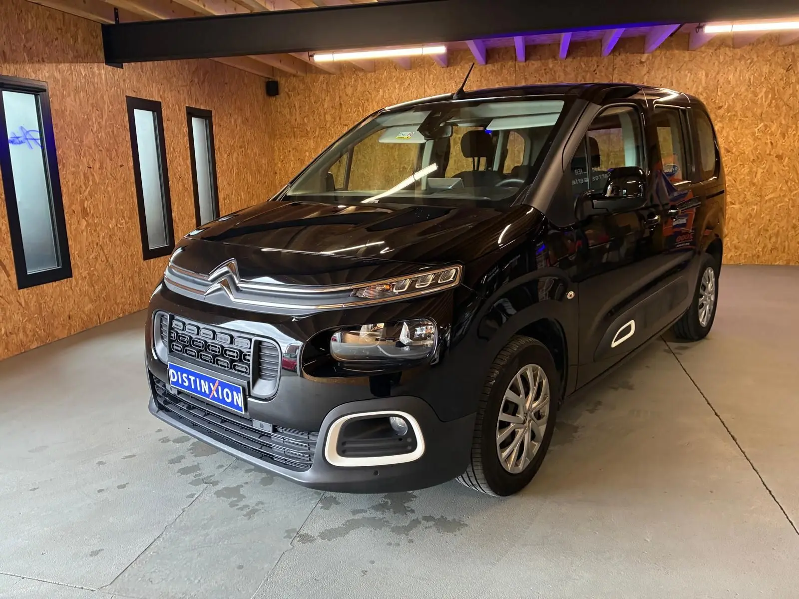 Vue 3/4 avant droit d'un Citroën Berlingo noir 2020, avec calandre distinctive et phares modernes dans un garage.