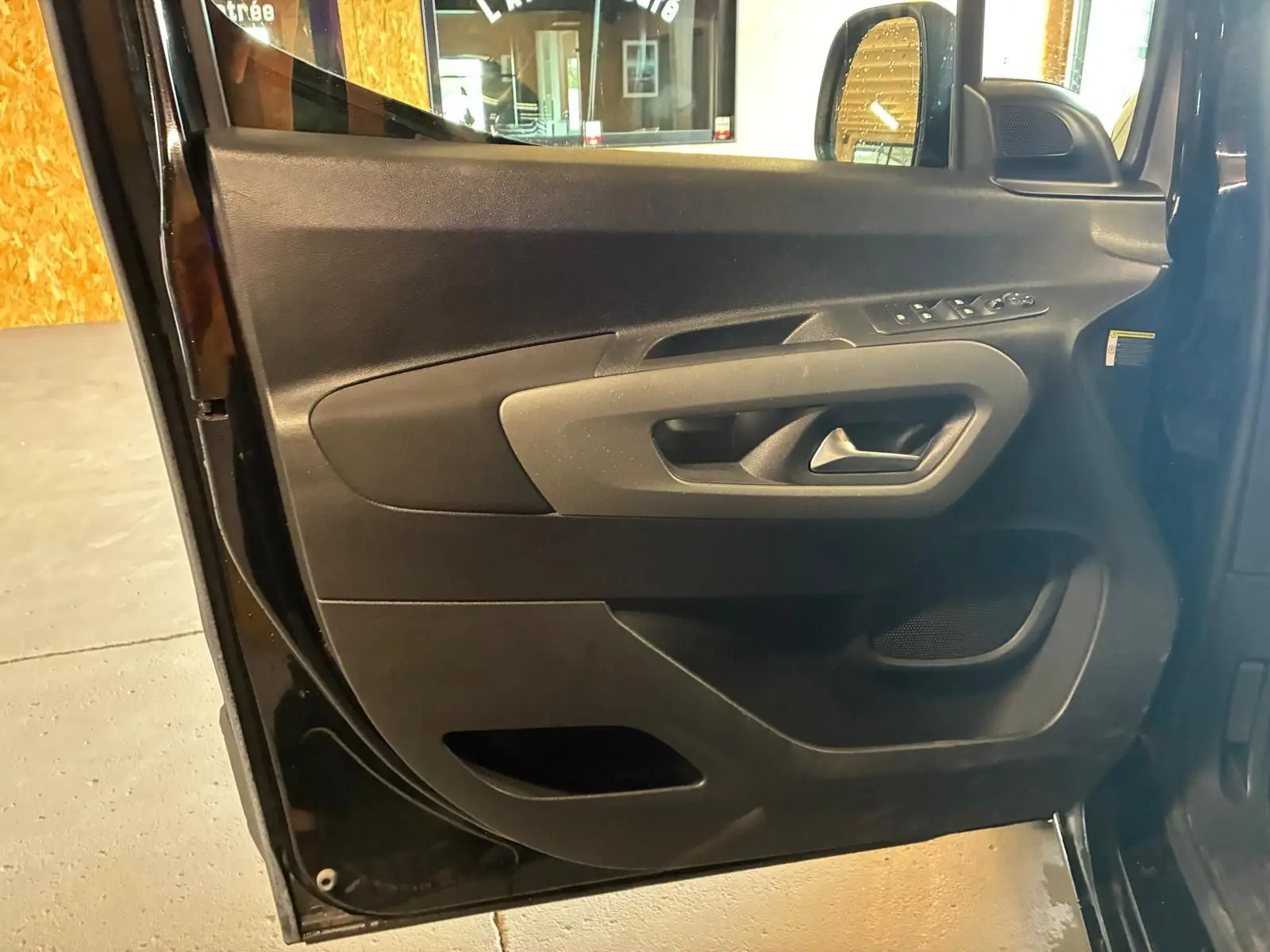 Vue rapprochée de la porte avant gauche noire du Citroën Berlingo 2020, montrant les commandes de vitres et la poignée intérieure.