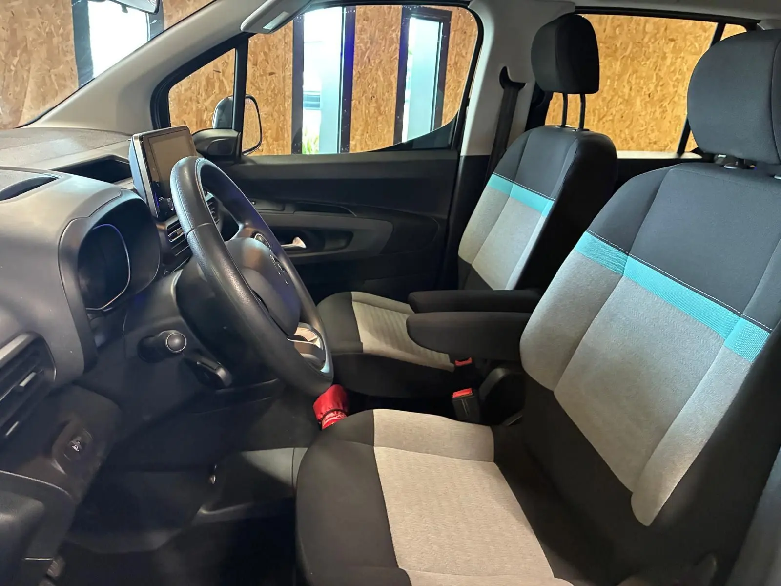 Vue intérieure côté conducteur du Citroën Berlingo noir 2020, sièges tissu gris et bleu avec volant et écran tactile.