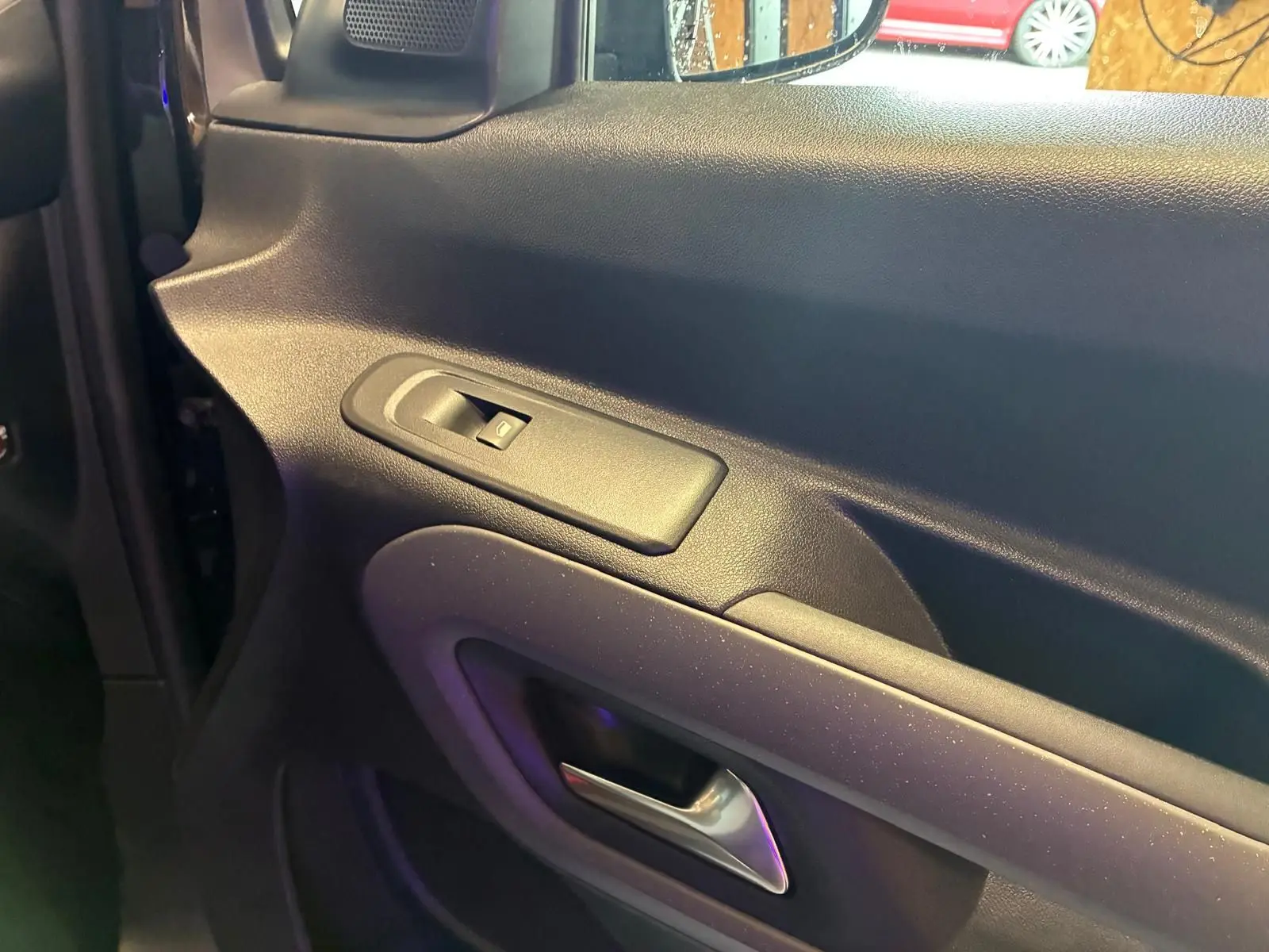 Détail de la porte intérieure côté gauche du Citroën Berlingo noir, avec commande de lève-vitre et poignée argentée.