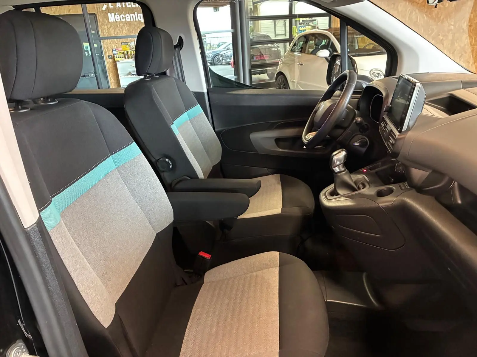 Vue intérieure côté conducteur du Citroën Berlingo noir 2020, montrant les sièges tissu gris et bleu et le tableau de bord avec écran tactile.