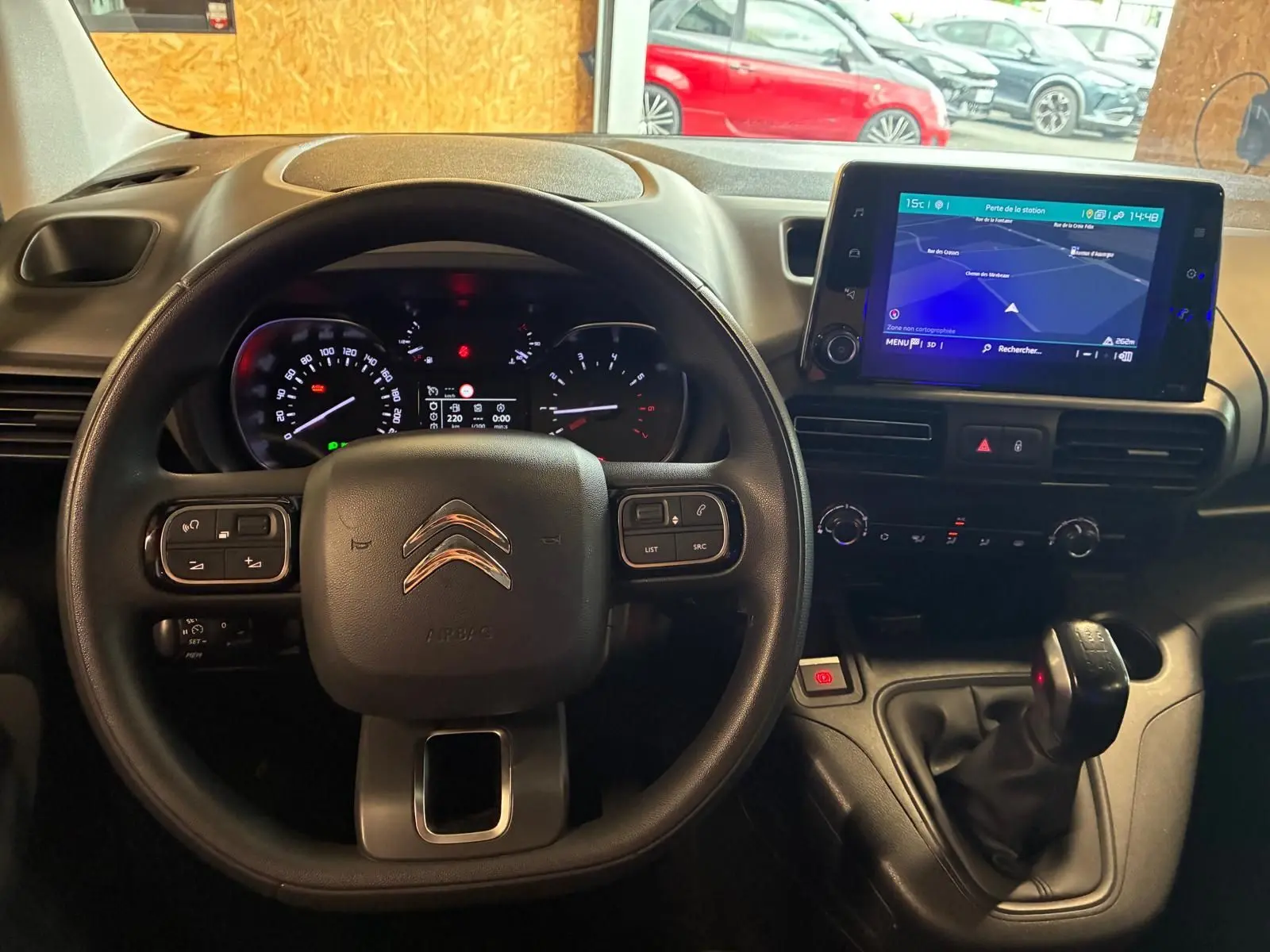 Vue intérieure centrée sur le volant et le tableau de bord du Citroën Berlingo noir avec écran tactile et levier de vitesses manuel.