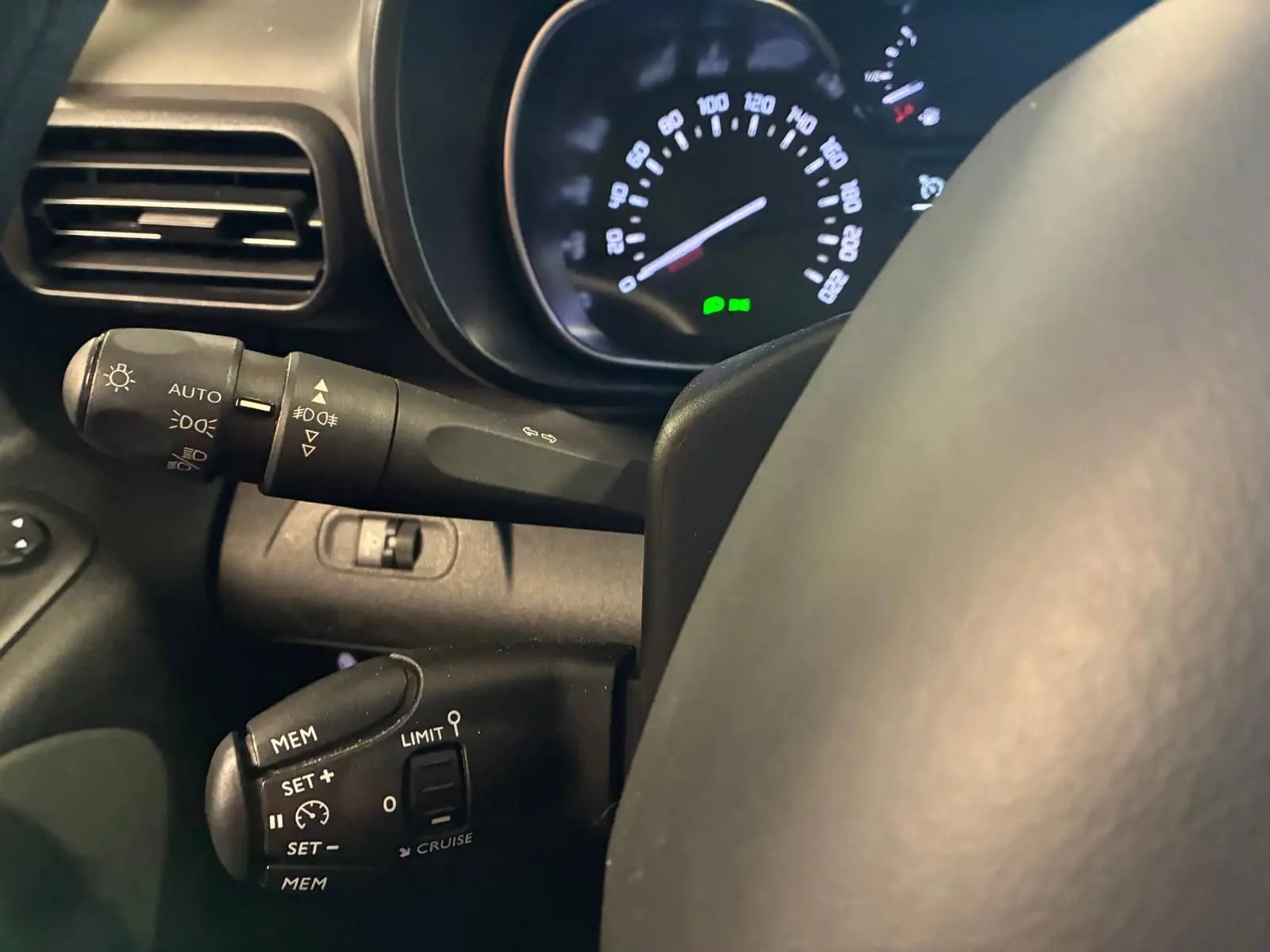 Gros plan sur le volant et les commandes de régulateur de vitesse d’un Citroën Berlingo noir, tableau de bord en arrière-plan.
