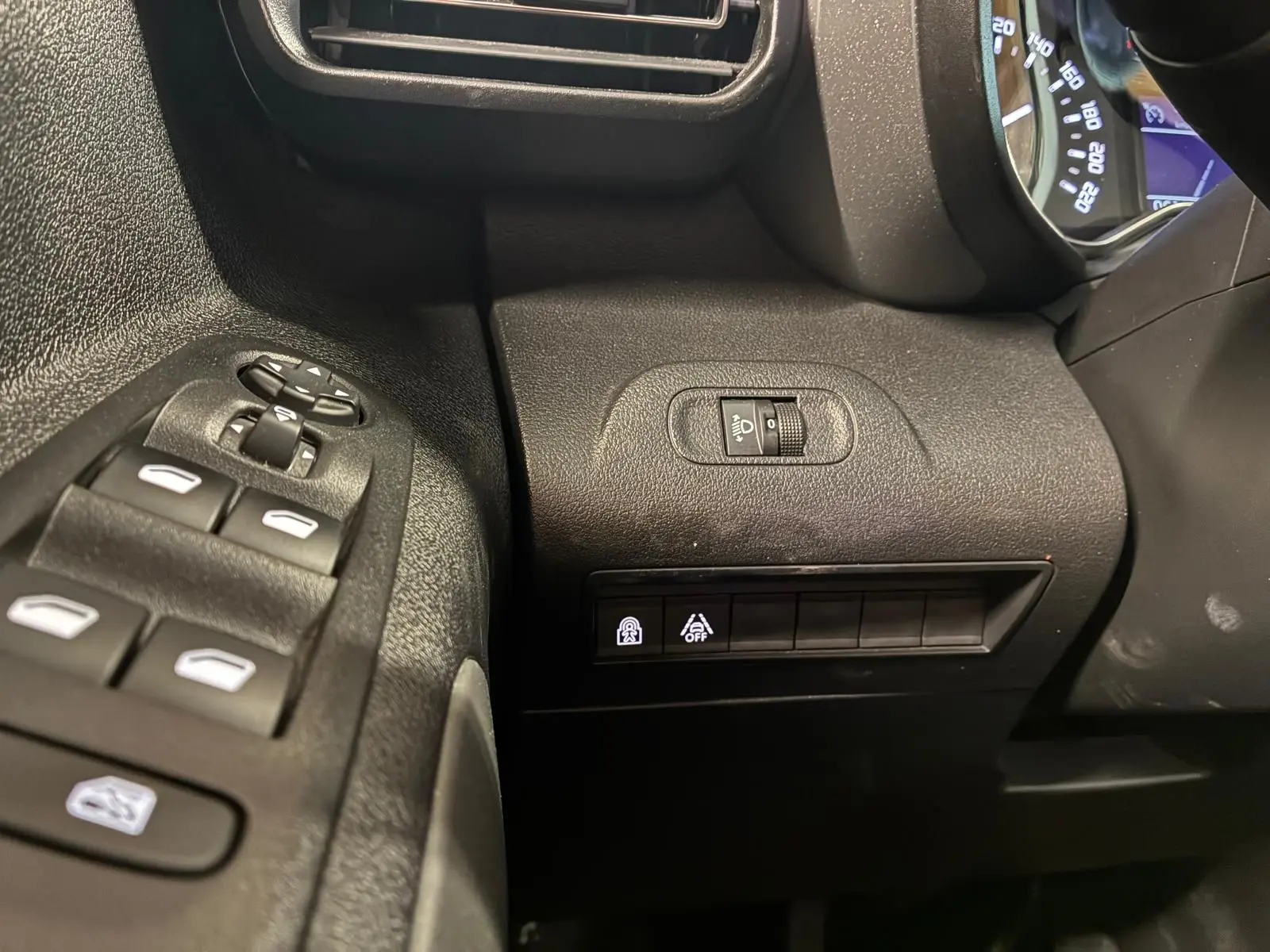 Détail intérieur côté gauche du tableau de bord noir du Citroën Berlingo 2020 avec commandes de vitres et réglage phares.