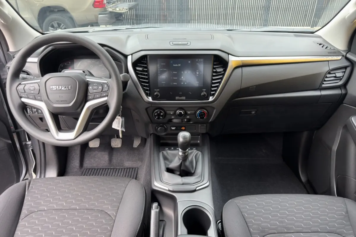 Vue intérieure avant du tableau de bord et volant multifonctions du pick-up Isuzu D-MAX avec sellerie tissu noire.