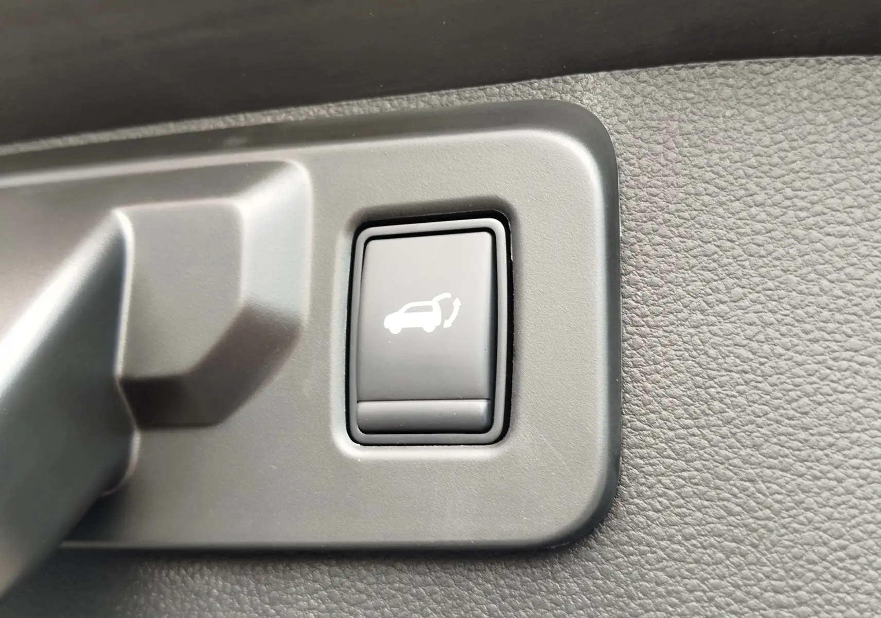 Bouton noir intérieur de Renault Symbioz 2026 pour ouverture électrique du hayon, entouré de plastique gris texturé.