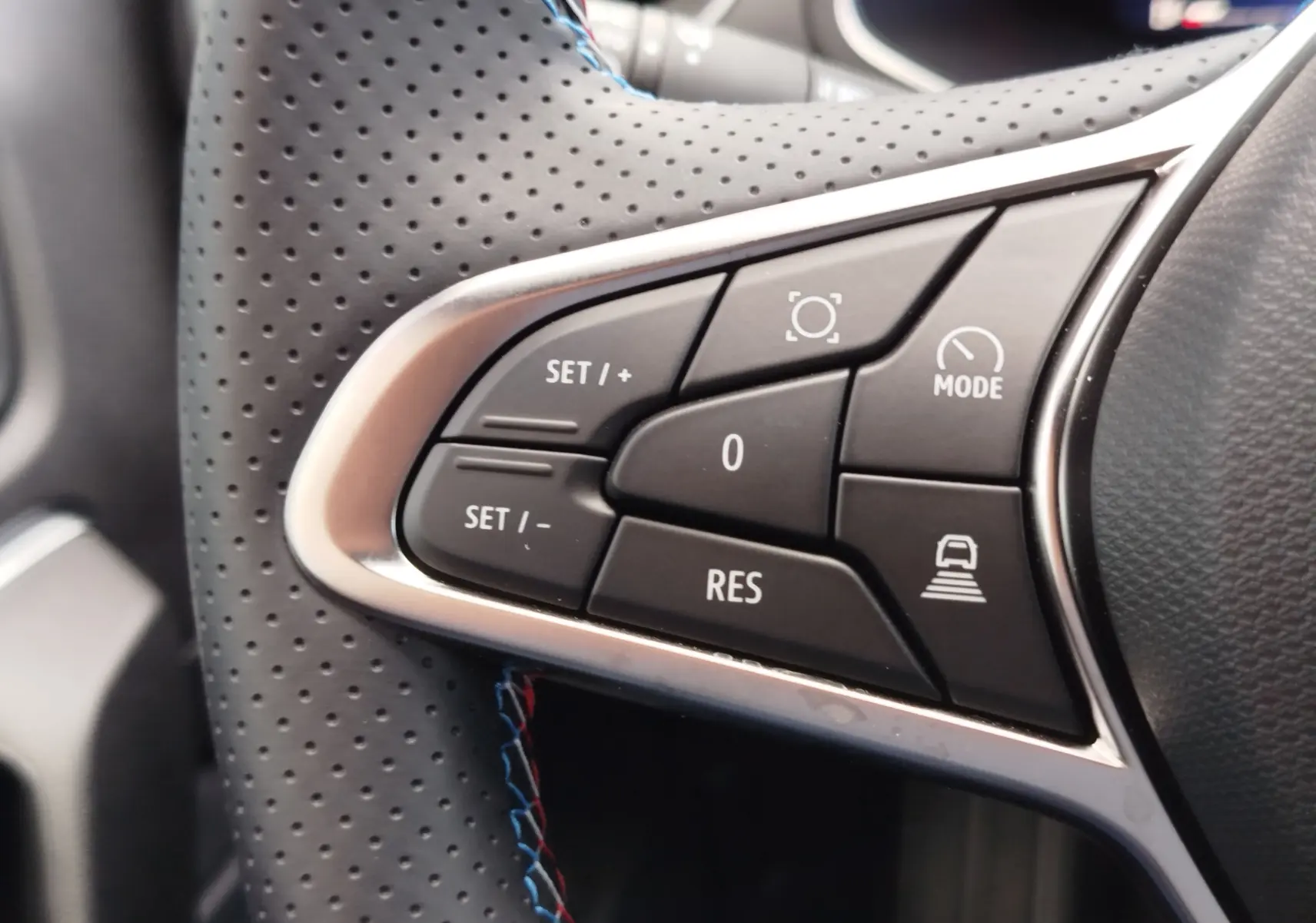 Gros plan sur les commandes noires du volant perforé avec surpiqûres bleues et rouges du Renault Symbioz gris cassiopée.