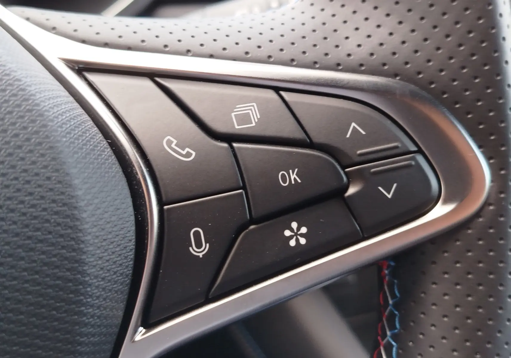 Gros plan sur les commandes multifonctions noires du volant perforé du Renault Symbioz gris Cassiopée, avec touches téléphone et micro.