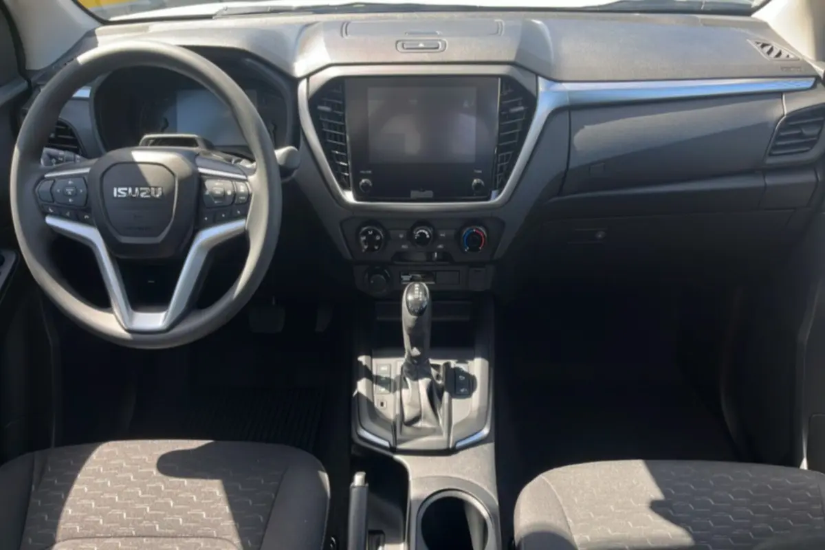 Vue intérieure avant de l'Isuzu D-MAX 2026, tableau de bord noir avec écran tactile et volant multifonctions.