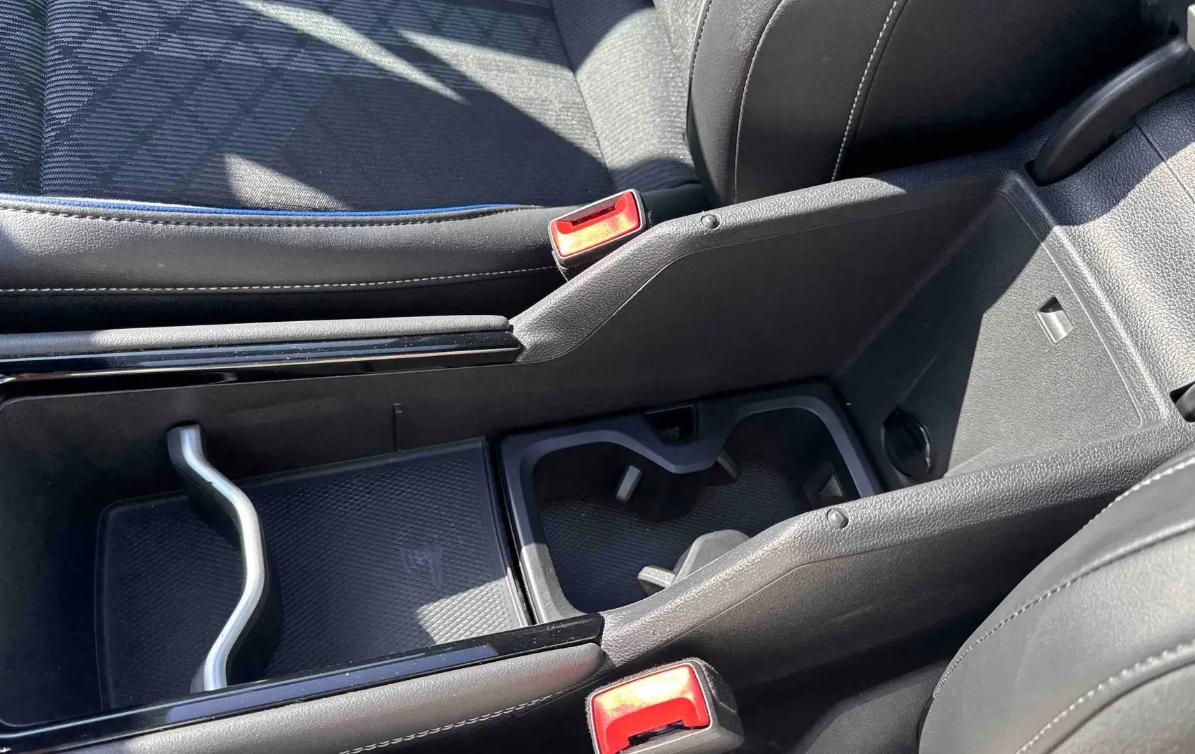 Gros plan sur la console centrale noire du Volkswagen Tiguan 2025, montrant les porte-gobelets et le rangement intérieur.