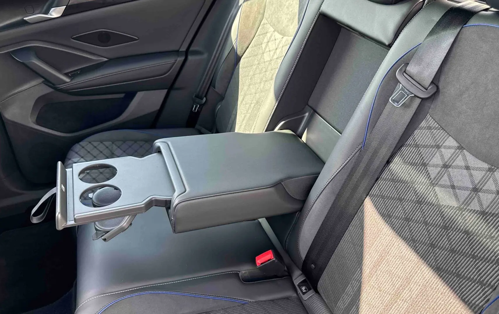 Vue rapprochée des sièges arrière noirs avec accoudoir central déployé et porte-gobelets du Volkswagen Tiguan 2025.