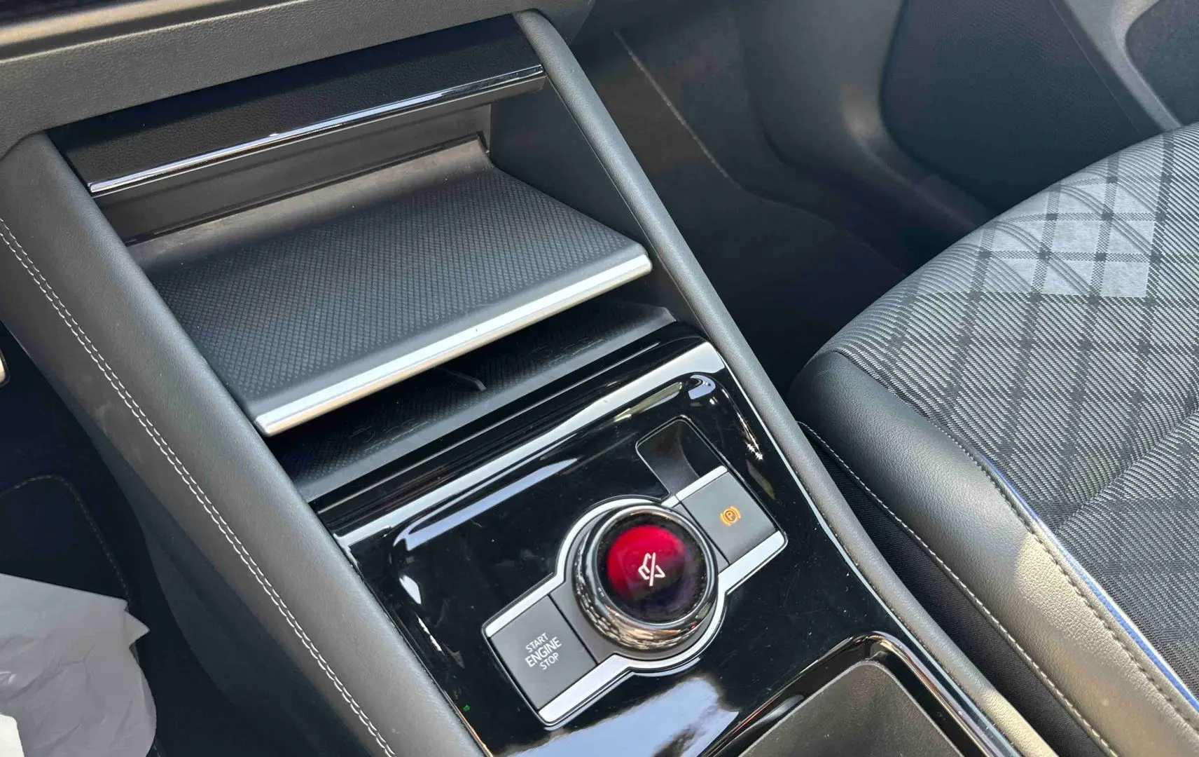 Vue rapprochée de la console centrale noire brillante avec bouton rotatif et siège avant gris à motifs du Volkswagen Tiguan 2025.