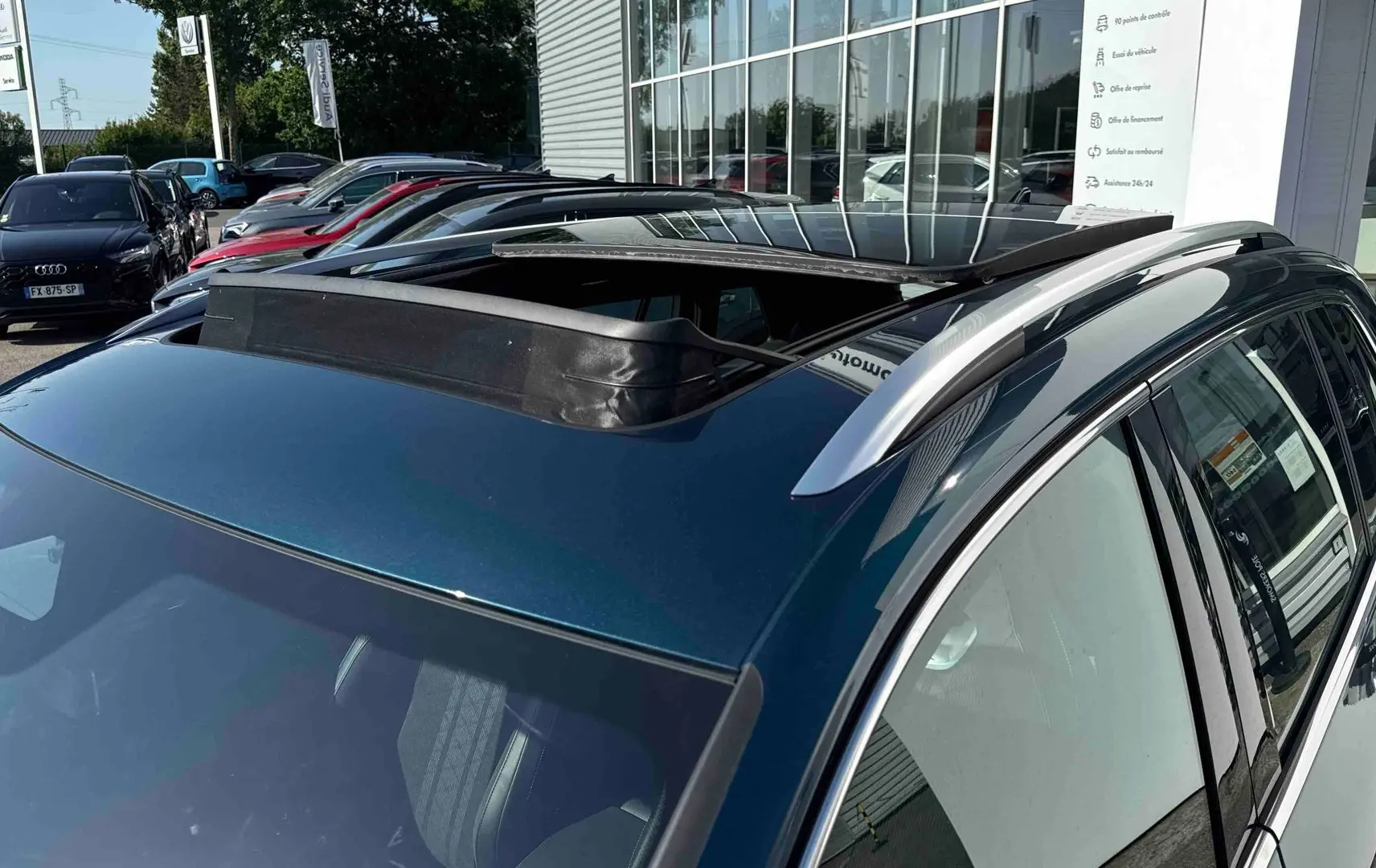 Vue 3/4 arrière droite du Volkswagen Tiguan bleu 2025 avec toit ouvrant panoramique et barres de toit argentées.