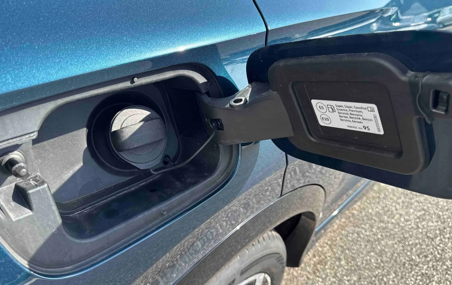 Bouchon de réservoir essence ouvert sur le côté gauche d’un Volkswagen Tiguan bleu métallisé, avec jante visible.