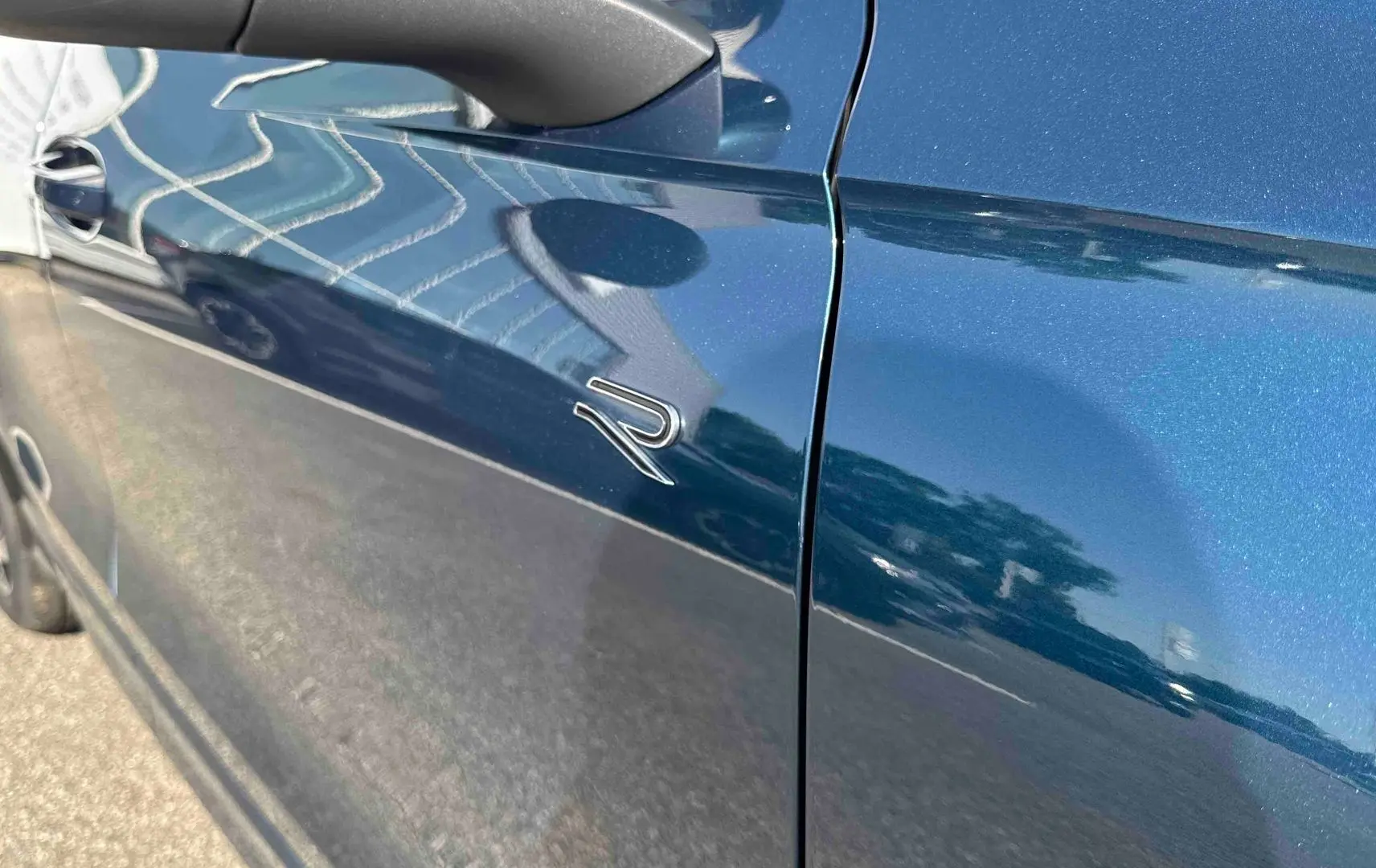 Vue rapprochée du côté gauche bleu métallisé du Volkswagen Tiguan 2025 avec logo R distinctif sur la porte.