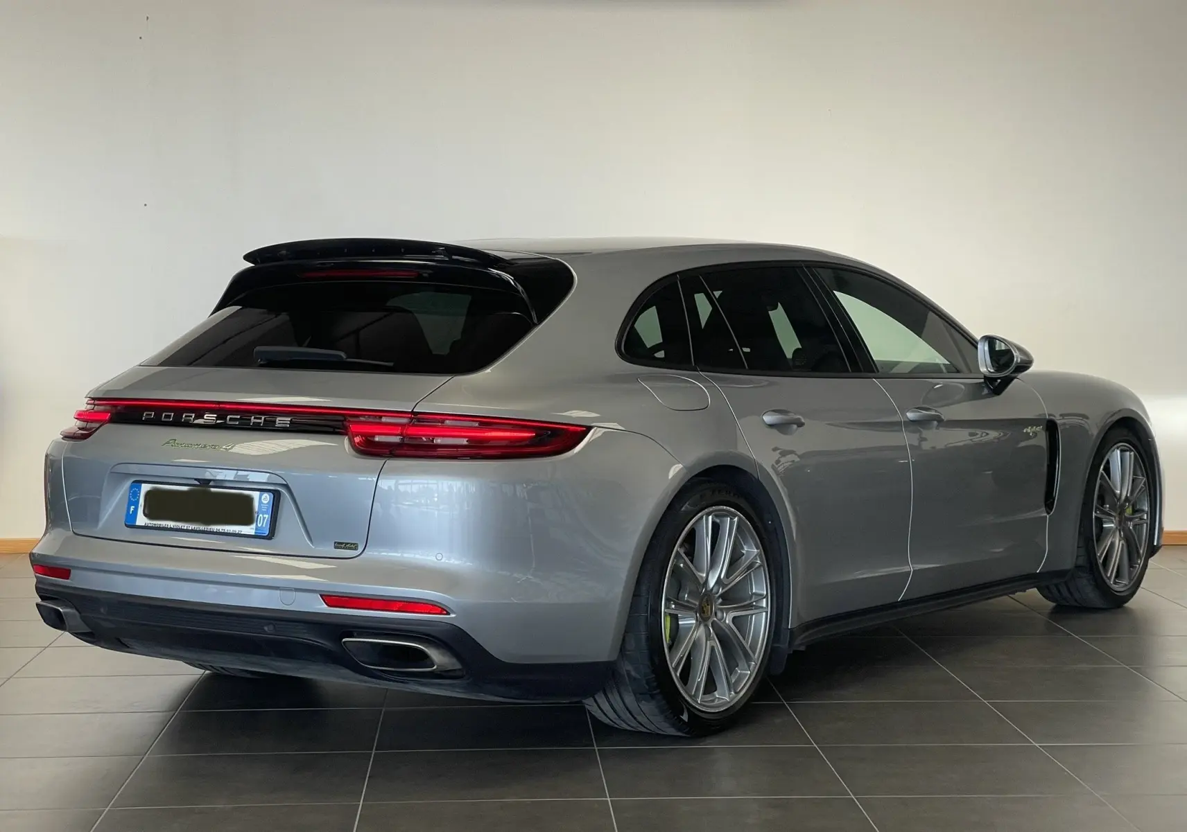 Porsche Panamera Sport Turismo gris vue 3/4 arrière droit, avec feux arrière allongés et jantes alliage distinctives.