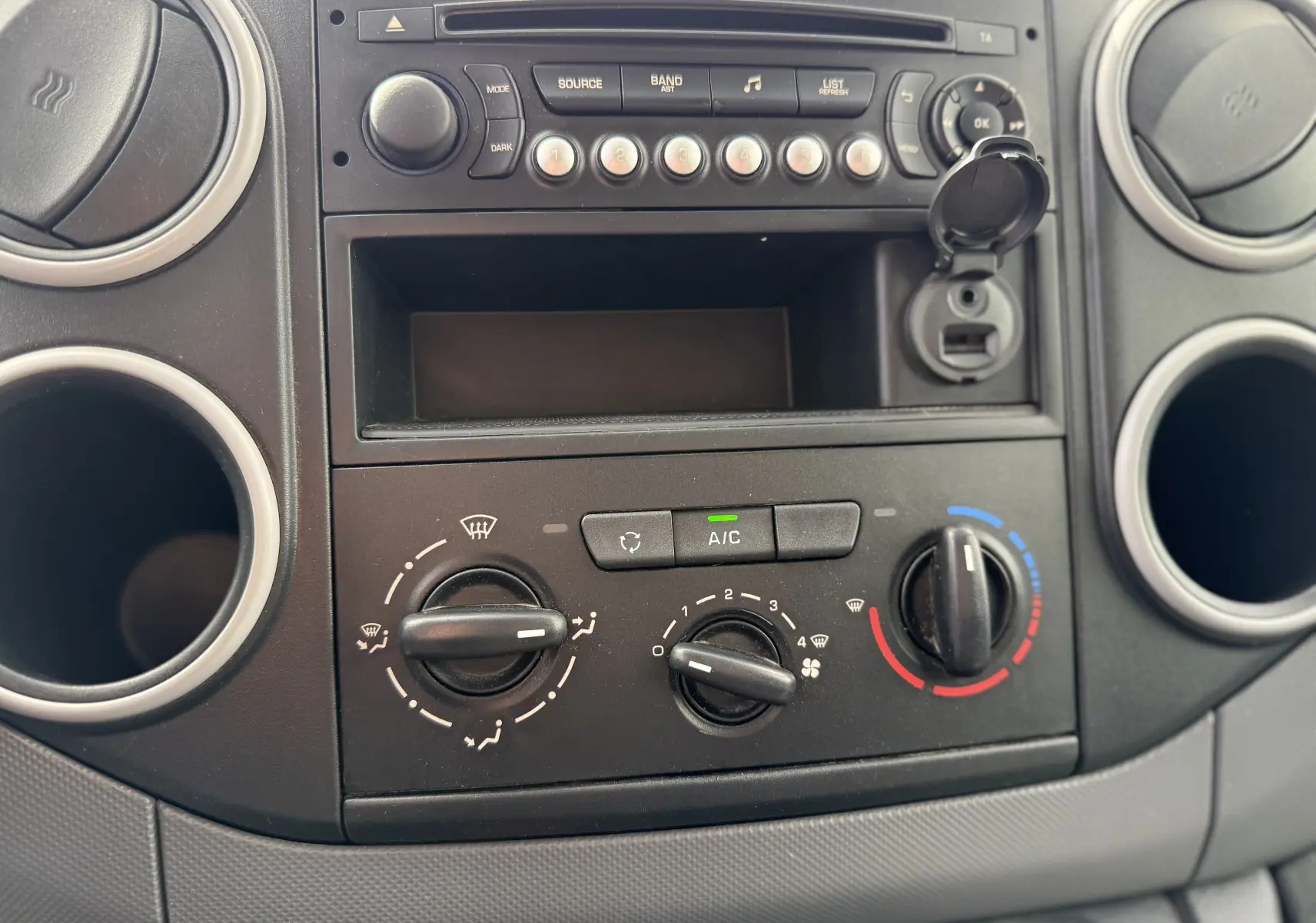 Vue rapprochée du tableau de bord du Peugeot Partner blanc 2017, montrant les commandes de climatisation et la radio.