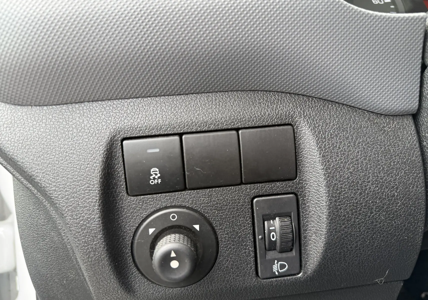 Gros plan sur les commandes de réglage des rétroviseurs et des phares du tableau de bord d’un Peugeot Partner blanc de 2017.