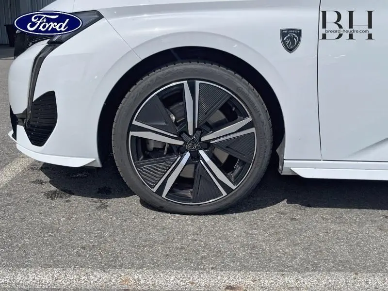 Gros plan sur la roue avant gauche et l'aile blanche Okénite d'une Peugeot 308 SW PHEV 180ch GT avec logo lion noir.