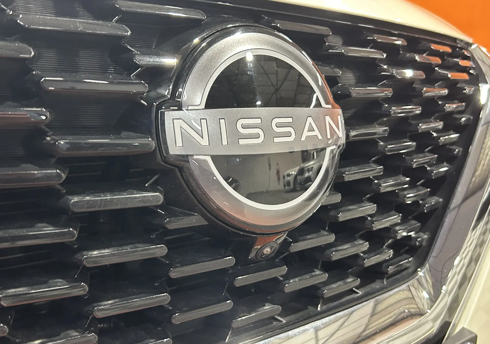 Gros plan sur la calandre noire et le logo Nissan argenté du Qashqai blanc lunaire avec caméra frontale intégrée.
