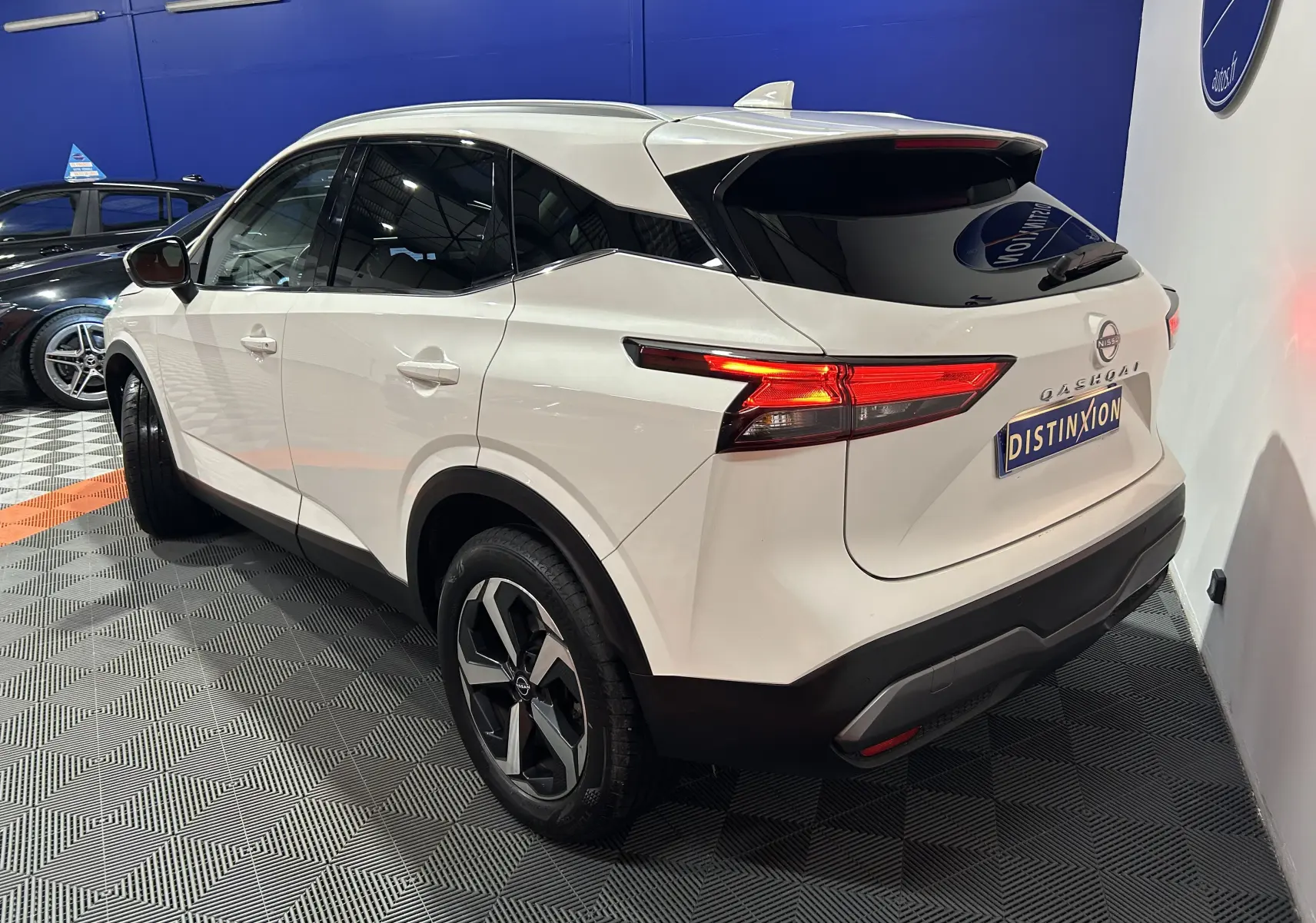 Vue 3/4 arrière droite du Nissan Qashqai blanc lunaire avec feux LED allumés et toit panoramique visible.