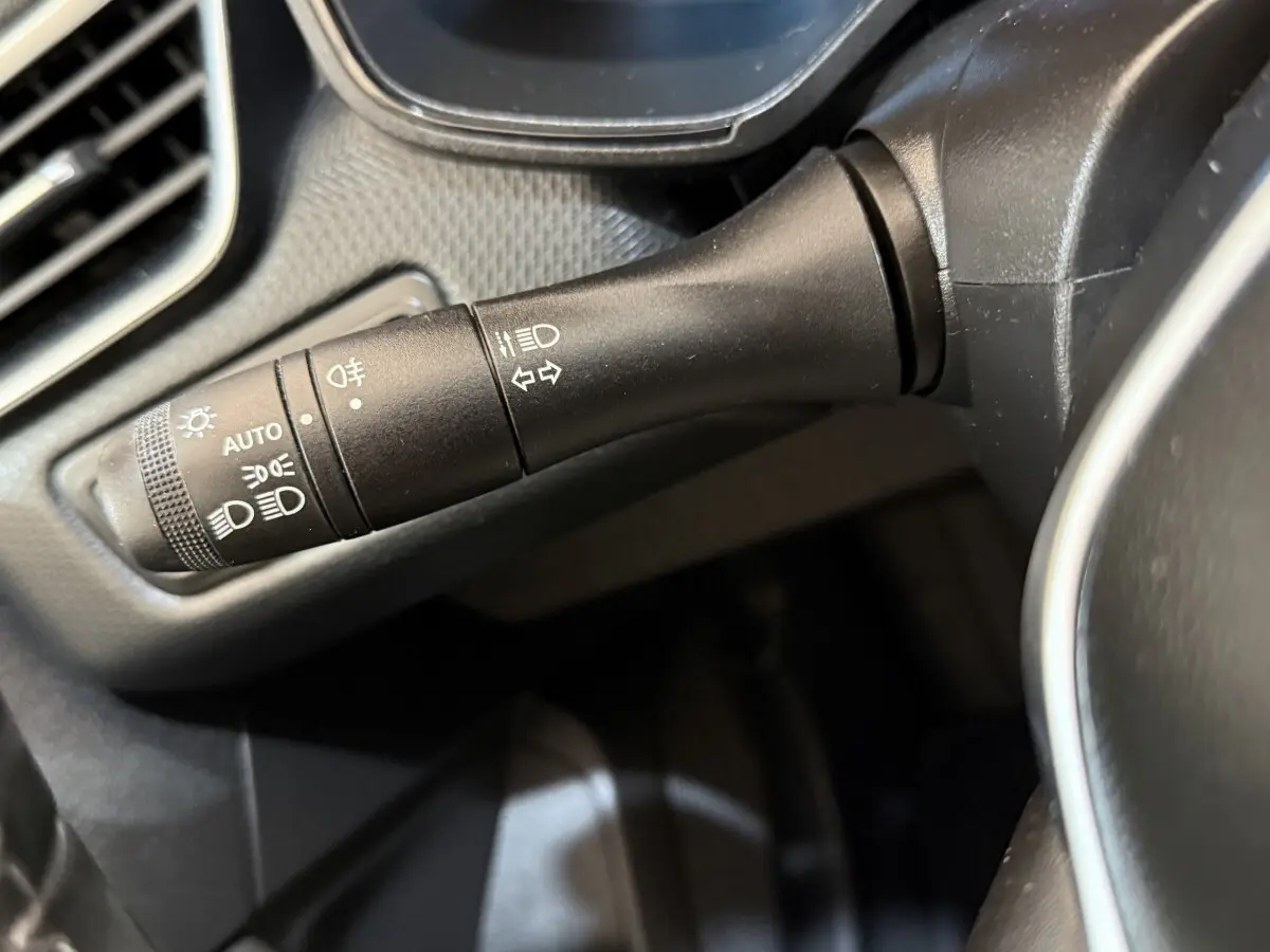 Gros plan sur la commande des phares et clignotants à gauche du volant dans une Renault Clio Business E-Tech hybride gris clair.