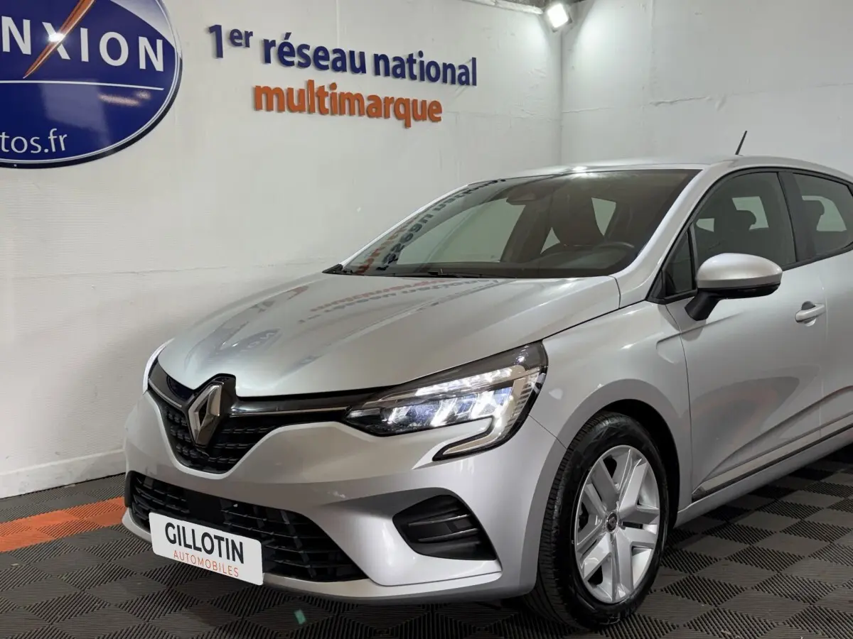 Renault Clio Business E-Tech hybride gris clair vue 3/4 avant droit avec phares LED allumés en showroom.