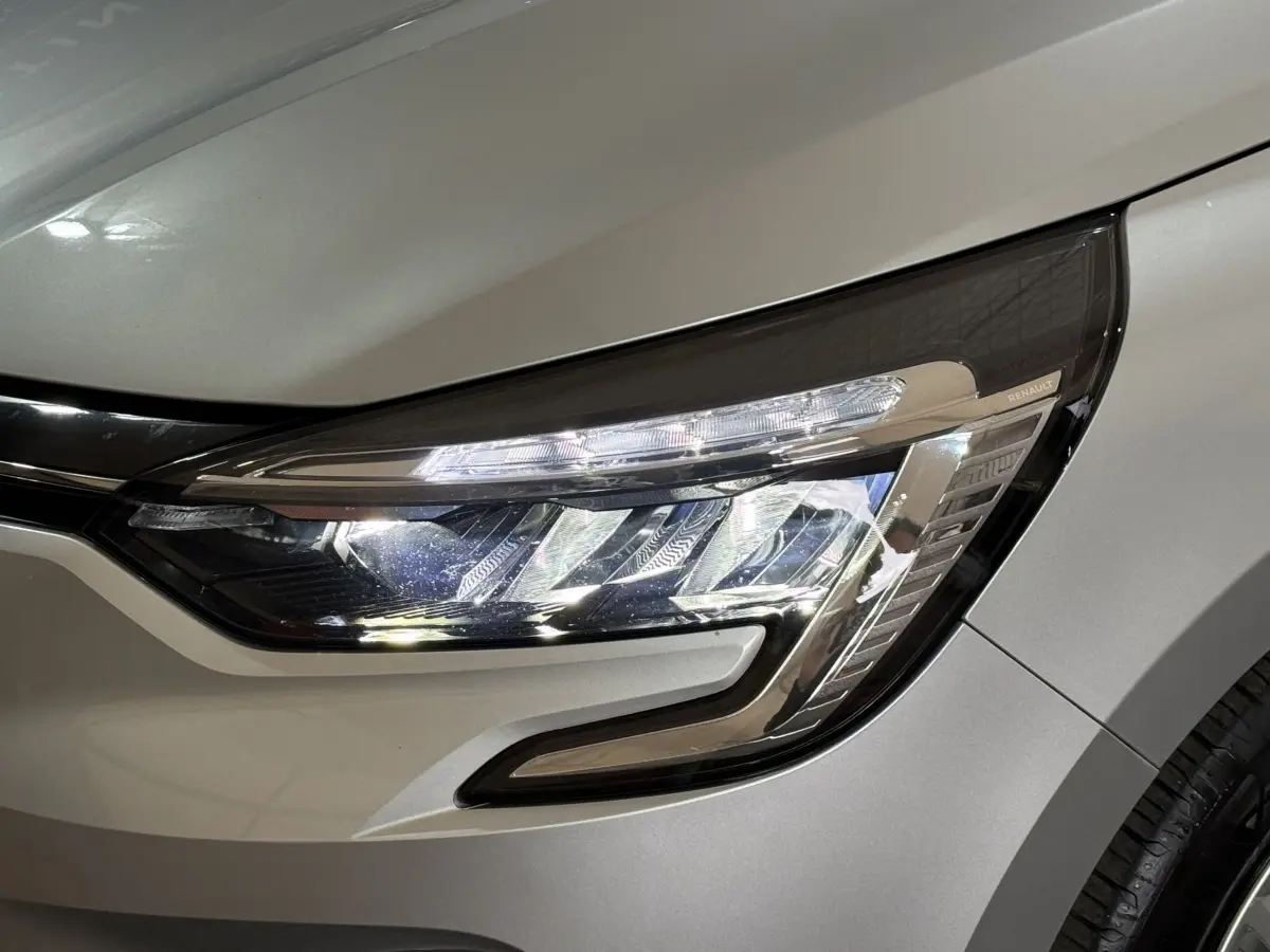Gros plan sur le phare avant droit d’une Renault Clio Business E-Tech hybride gris clair, soulignant ses LED et détails chromés.
