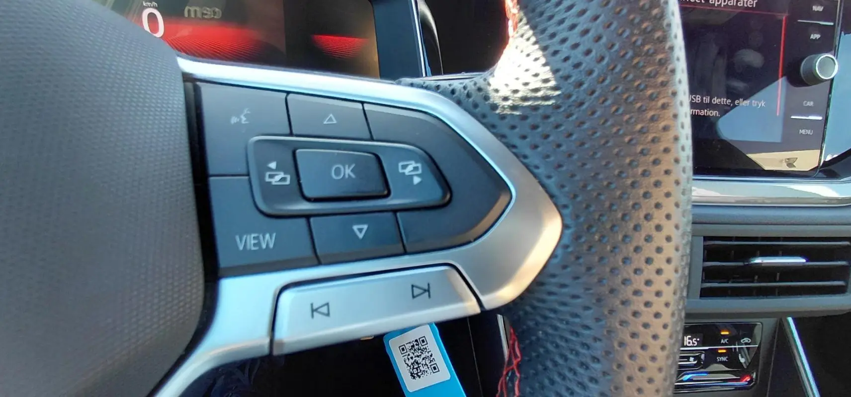 Gros plan sur le volant sport perforé côté gauche du Volkswagen Polo GTI noir avec commandes intégrées et écran digital.