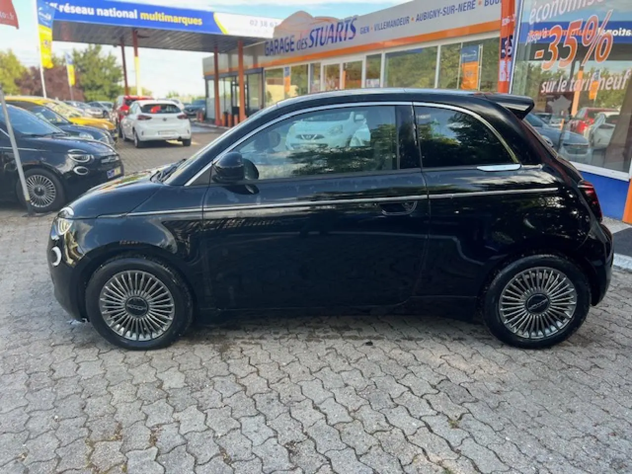 Profil côté gauche d'une FIAT 500 électrique noire 2022, avec jantes stylisées et poignées de porte discrètes.