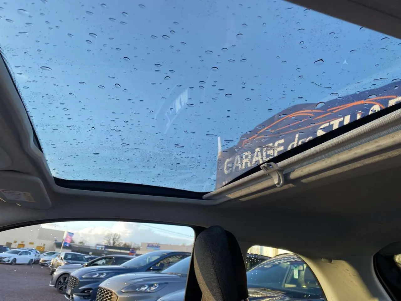 Toit vitré panoramique avec gouttes d'eau sur une Fiat 500 électrique noire, vue intérieure côté arrière droit.
