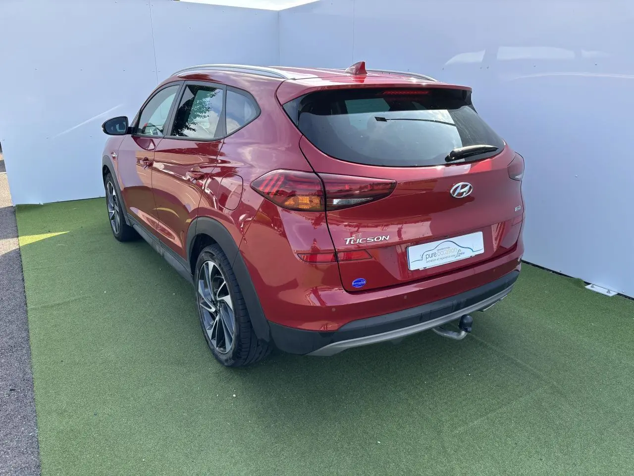 Vue 3/4 arrière droite d'un Hyundai Tucson rouge métallisé avec attelage et jantes alliage 17 pouces.