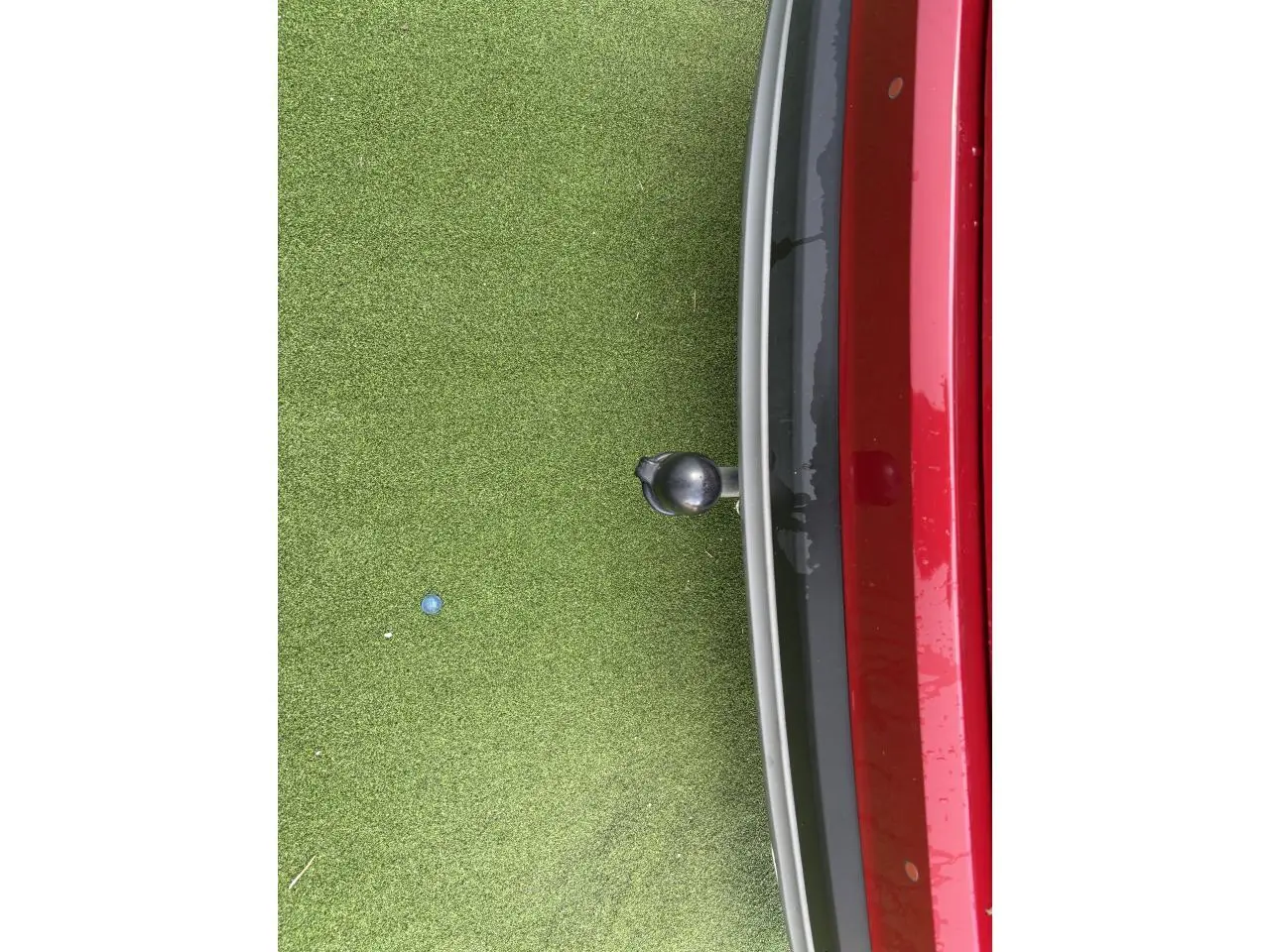 Vue rapprochée de l'arrière droit d'un Hyundai Tucson rouge métallisé avec attelage sur fond d'herbe synthétique.