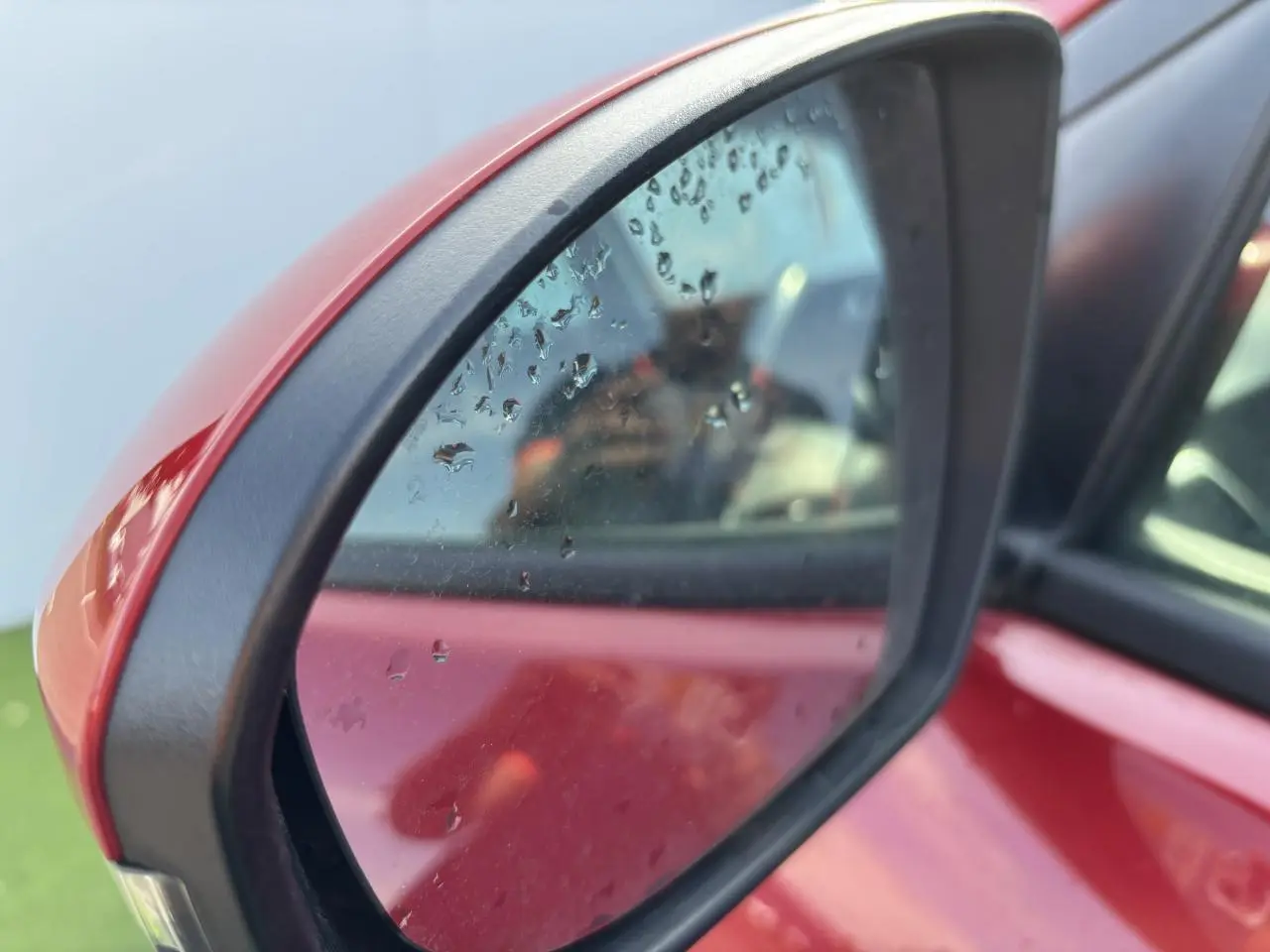 Rétroviseur extérieur côté gauche rouge métallisé du Hyundai Tucson III 2020 avec gouttes d'eau visibles sur le miroir.