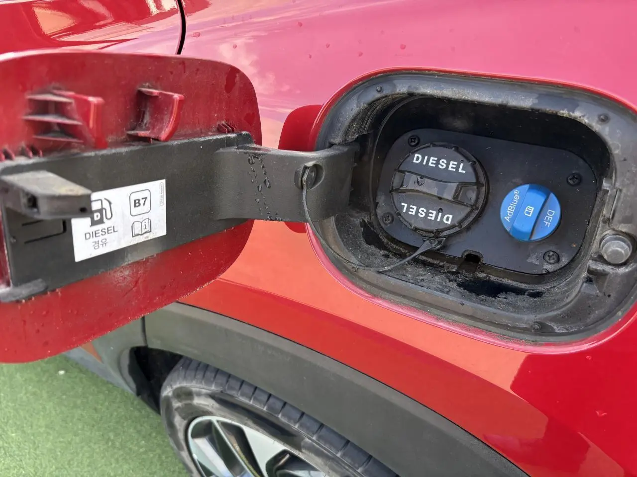 Gros plan sur la trappe à carburant côté gauche d'un Hyundai Tucson rouge métallisé, bouchons diesel et AdBlue visibles.
