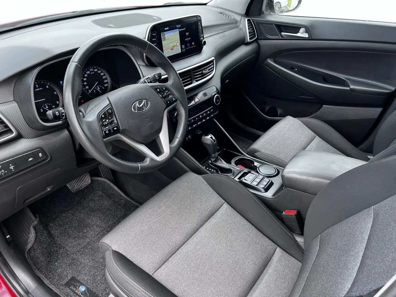 Intérieur avant droit du Hyundai Tucson III rouge métallisé, tableau de bord avec écran tactile et volant cuir multifonctions.