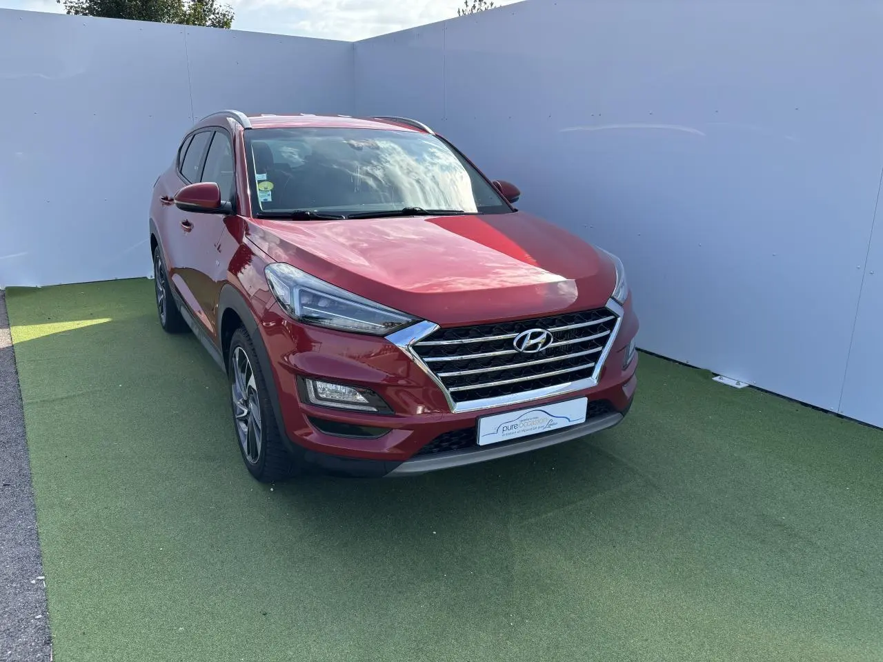 Vue 3/4 avant gauche d'un Hyundai Tucson rouge métallisé avec calandre chromée et jantes alliage.