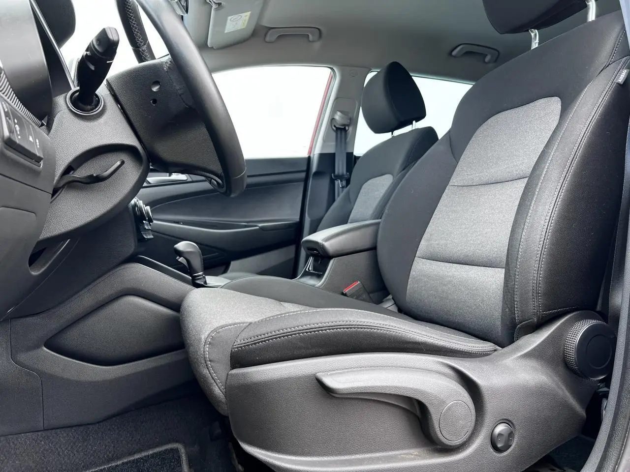 Vue intérieure côté conducteur du Hyundai Tucson III avec sièges tissu gris et accoudoir central noir.
