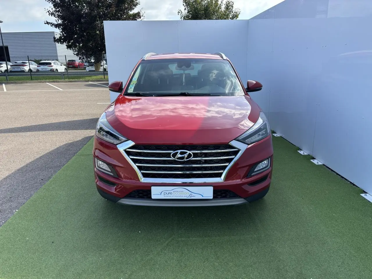 Vue frontale d'un Hyundai Tucson rouge métallisé avec calandre chromée et feux LED distinctifs.