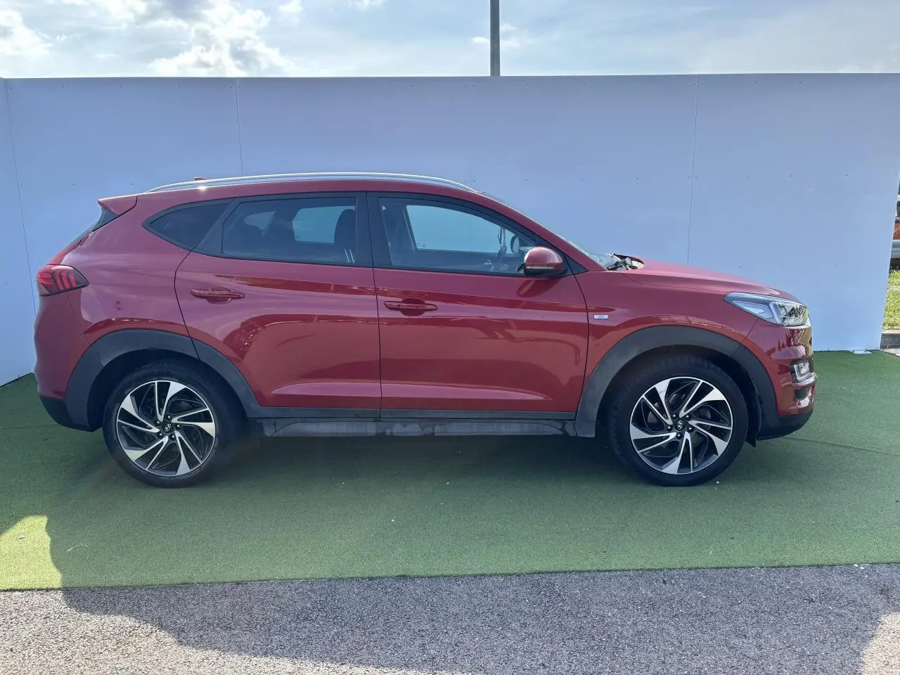 Profil droit d'un Hyundai Tucson rouge métallisé 2020 avec jantes alliage et vitres teintées sur fond neutre.