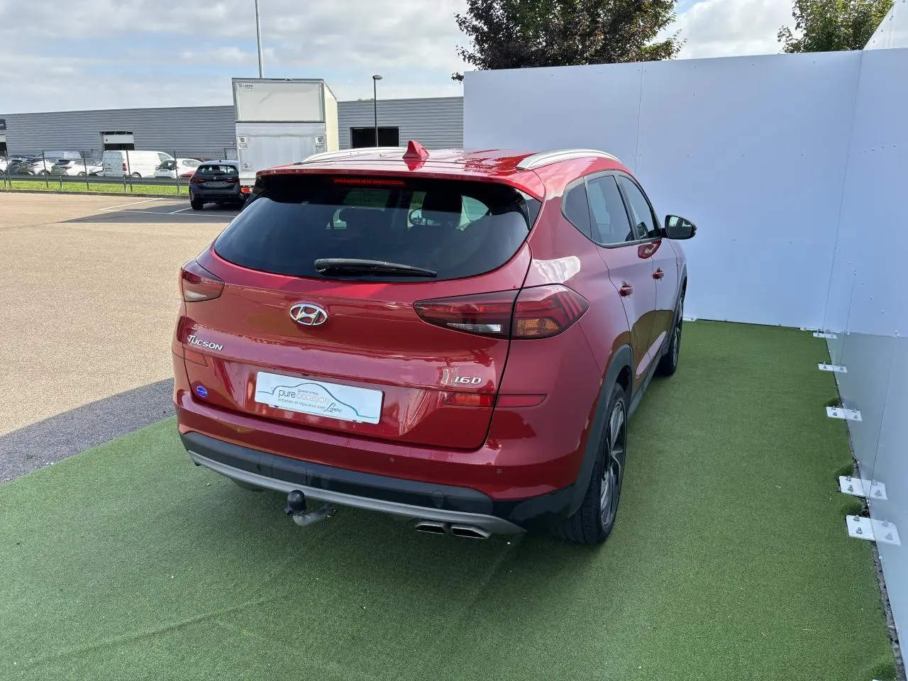 Vue 3/4 arrière droite d'un Hyundai Tucson rouge métallisé avec attelage et feux arrière LED visibles.