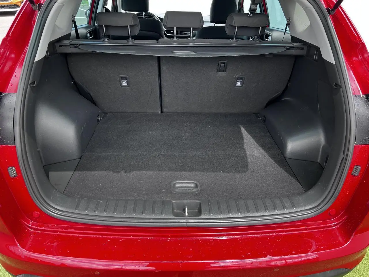 Coffre ouvert vu de l'arrière d'un Hyundai Tucson rouge métallisé, montrant l'espace de chargement et la plage arrière.