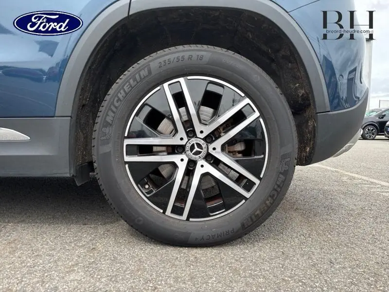 Gros plan sur la roue avant droite du Mercedes GLA 250 e bleu denim métallisé avec jante alu bicolore et logo étoile central.