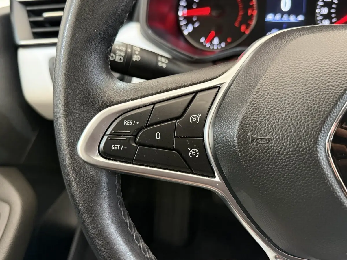 Gros plan sur le volant cuir synthétique de la Renault Clio blanc, avec commandes de régulateur de vitesse intégrées.