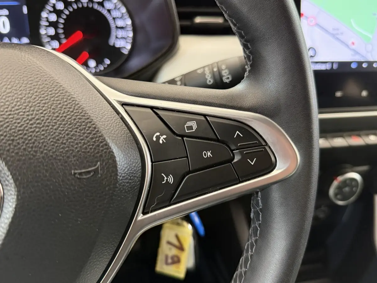 Gros plan sur le volant cuir synthétique de la Renault Clio blanc 2023, avec commandes multifonctions et tableau de bord partiel.