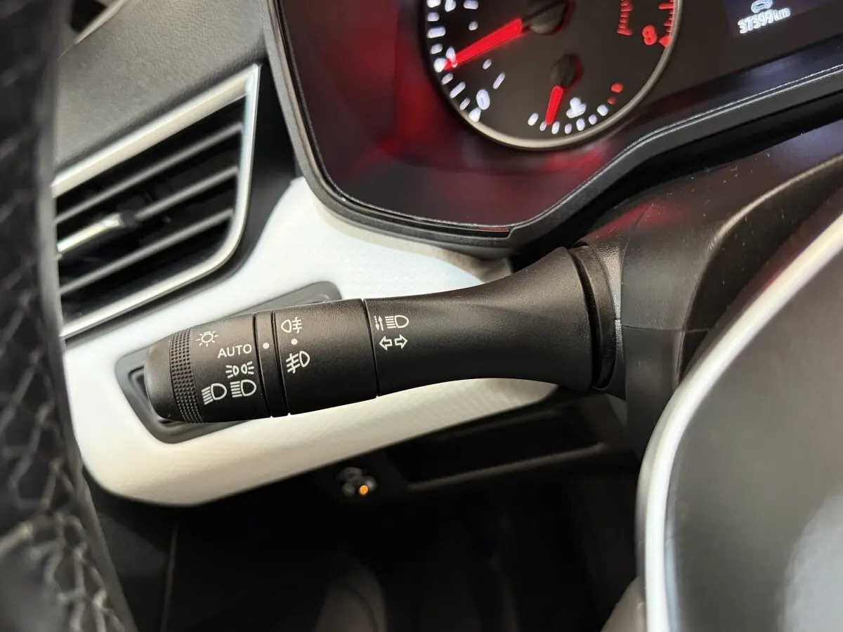 Gros plan sur la commande des phares et clignotants à gauche du volant dans l’habitacle d’une Renault Clio blanche.